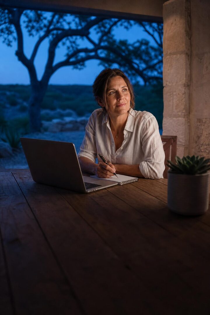 A business owner working on a laptop on a ranch porch at dusk