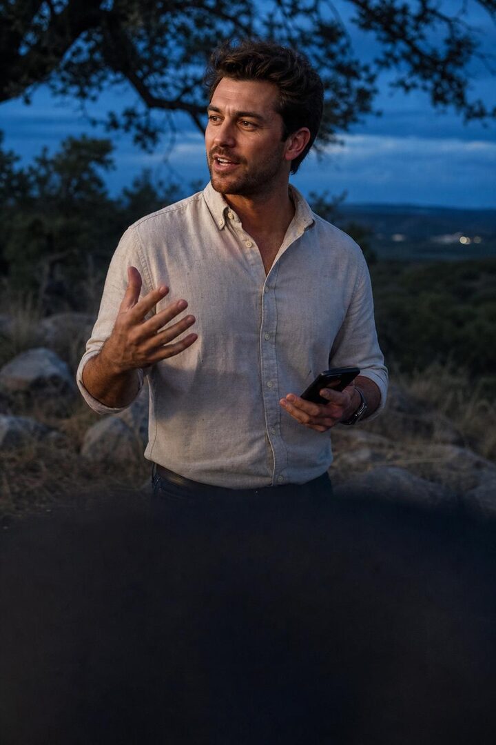 An entrepreneur talking with someone outdoors at dusk, phone in hand